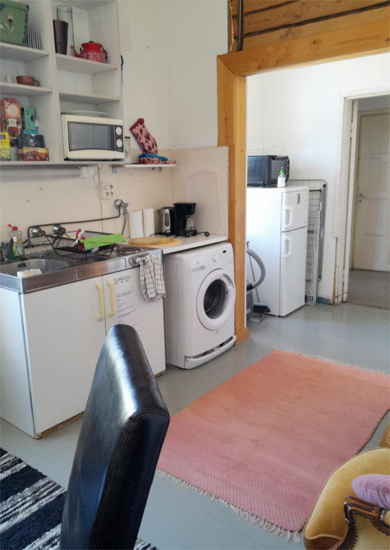 A kitchen with a washing machine, microwave and a fridge